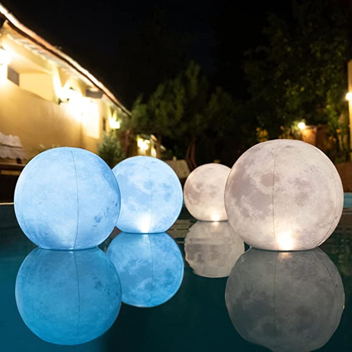 Moon-shaped and patterned lamps float in a swimming pool at nighttime. 