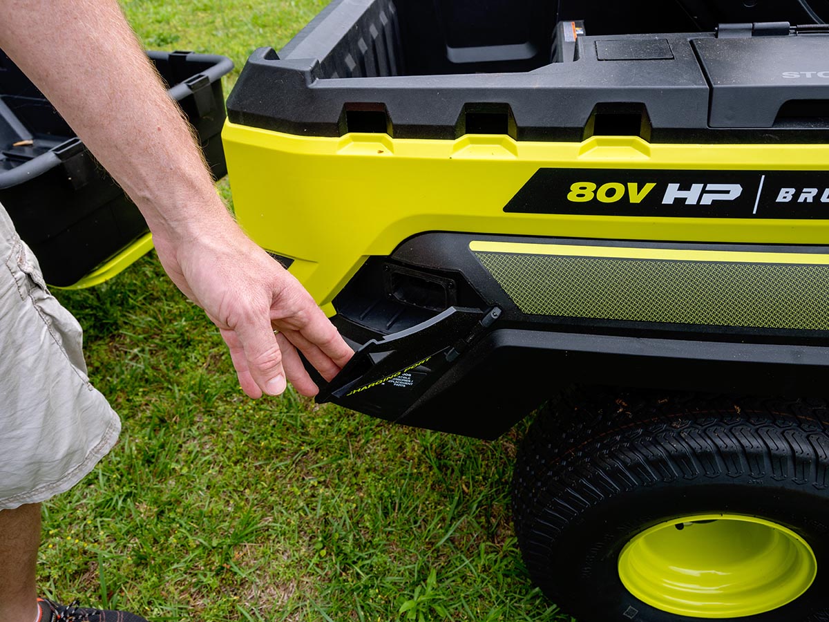 Person's hand opening door to charging port on Ryobi 80V HP Electric Lawn Tractor