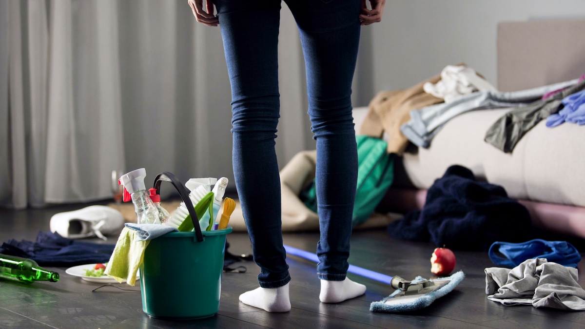 Woman standing in cluttered home with cleaning supplies