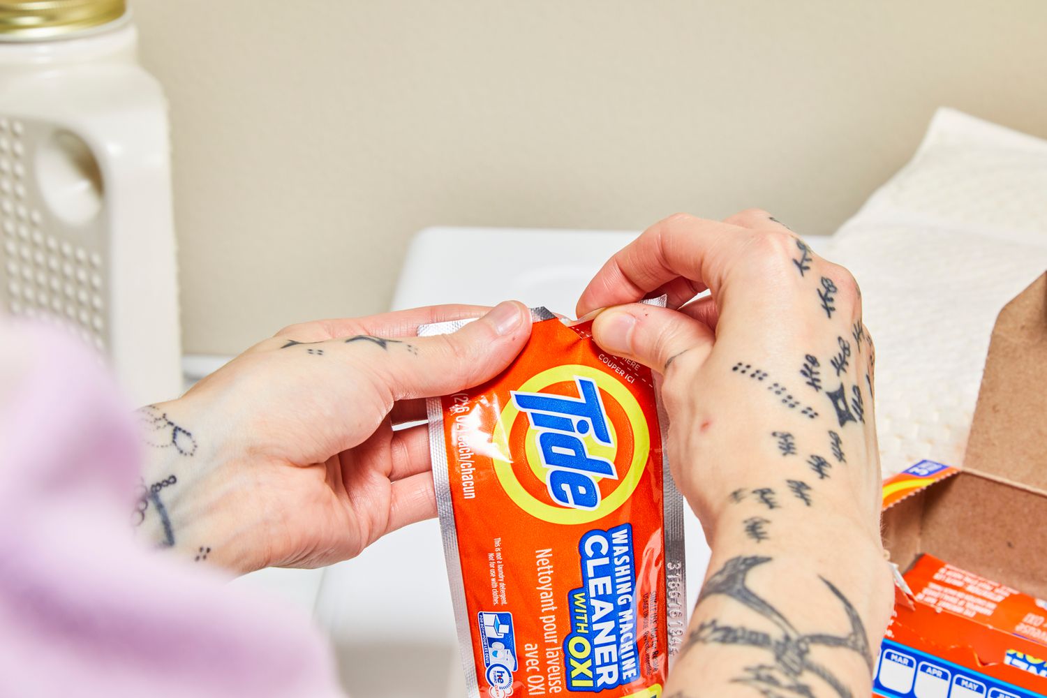 Hand opening a Tide Washing Machine Cleaner with Oxi packet.