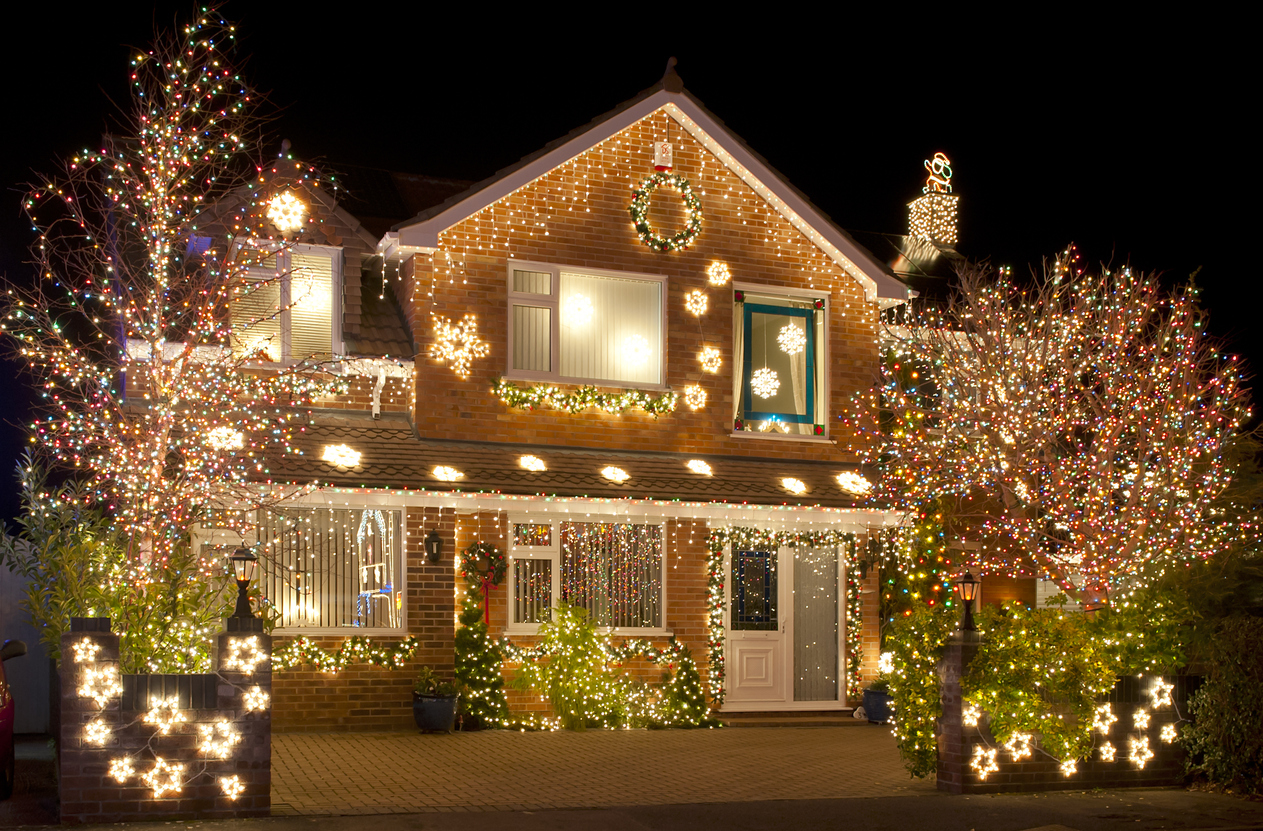 Une majestueuse maison en briques est décorée de lumières de Noël blanches et lumineuses suspendues autour du porche et bordant le toit et les arbres.