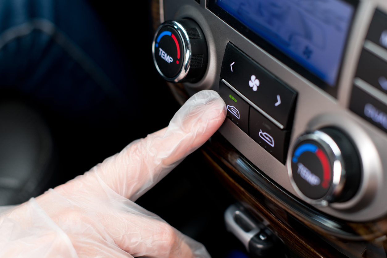 une main dans un gant médical appuie sur le bouton de recirculation de l'air dans la voiture