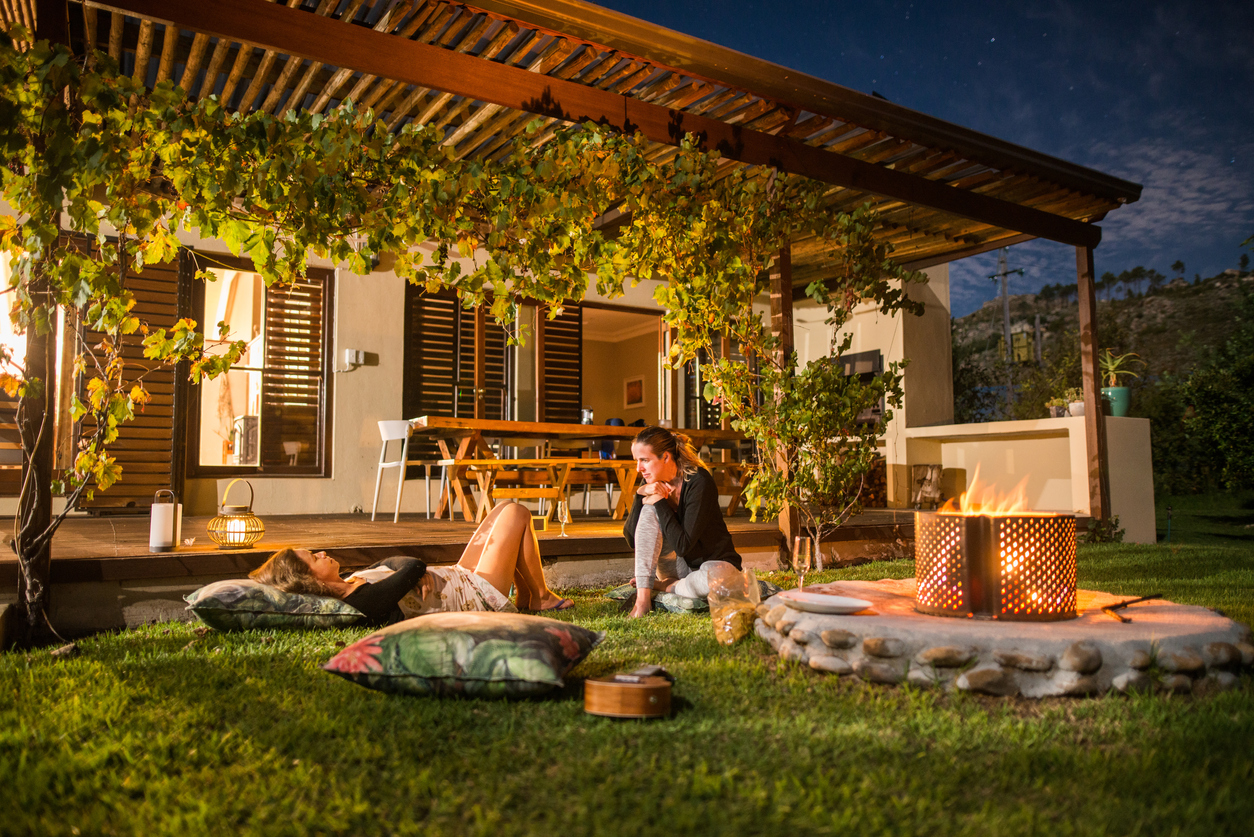 Two female friends talking over drinks while relaxing by a fire in their backyard in the evening