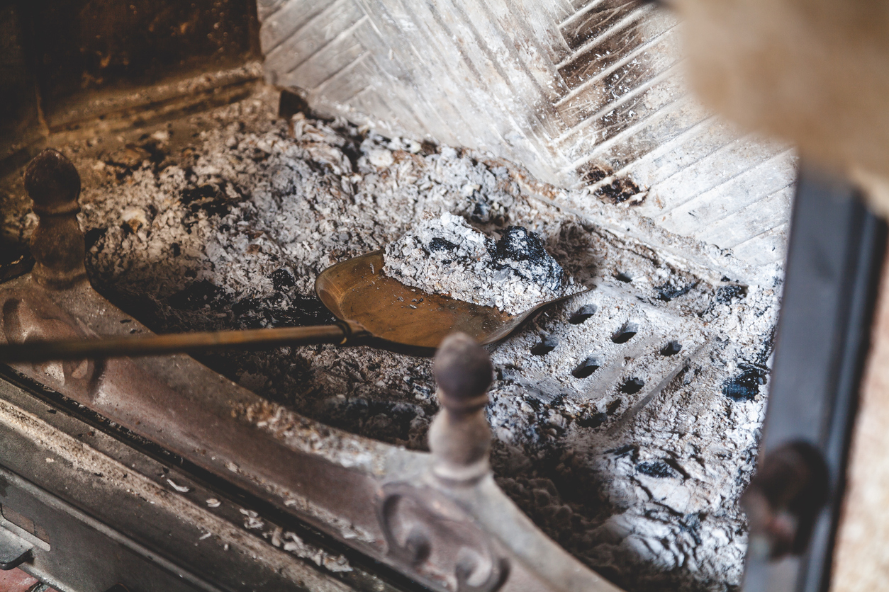 close shot of fireplace filled with ash and shovel scooping up grey ash