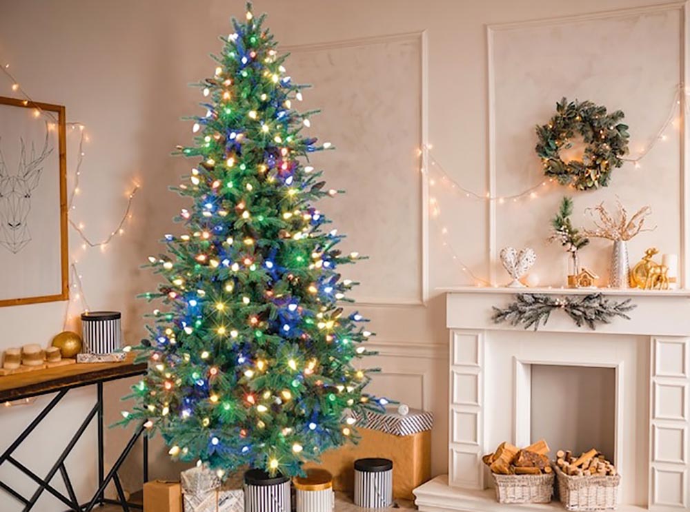 The GE Brunswick Fir Prelit Christmas Tree set up next to a fireplace in a neutral living room.