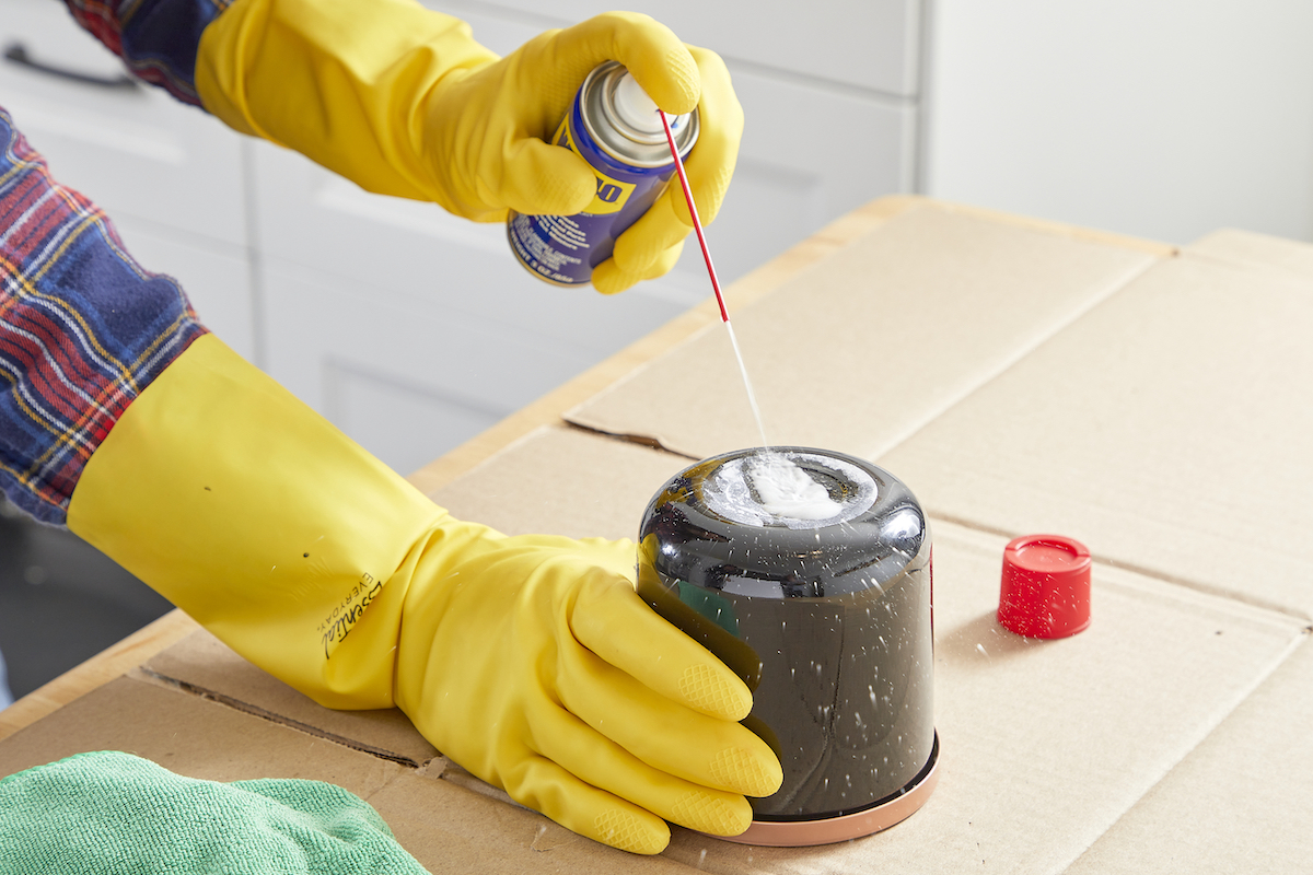 Woman sprays WD-40 to remove sticker on a jar.