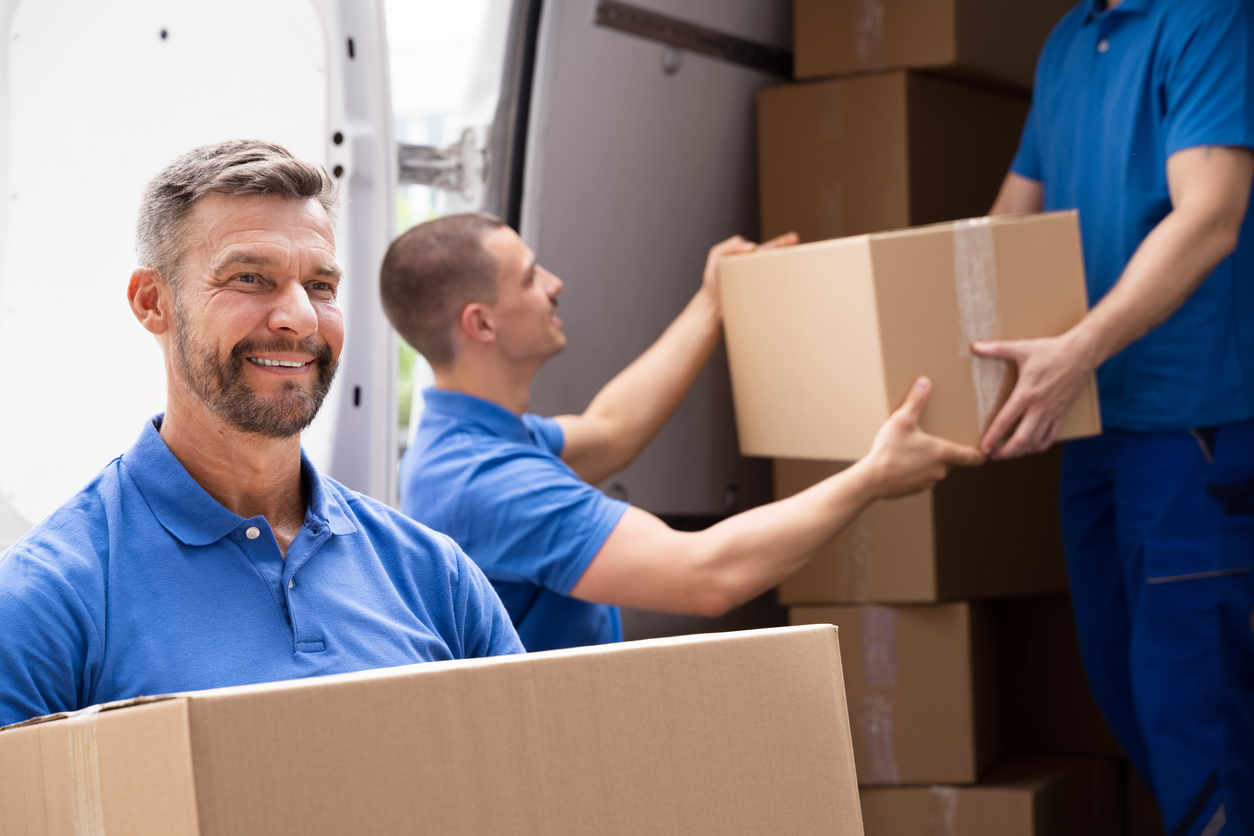 déménageurs professionnels en polo bleu tenant des cartons et les chargeant dans un camion