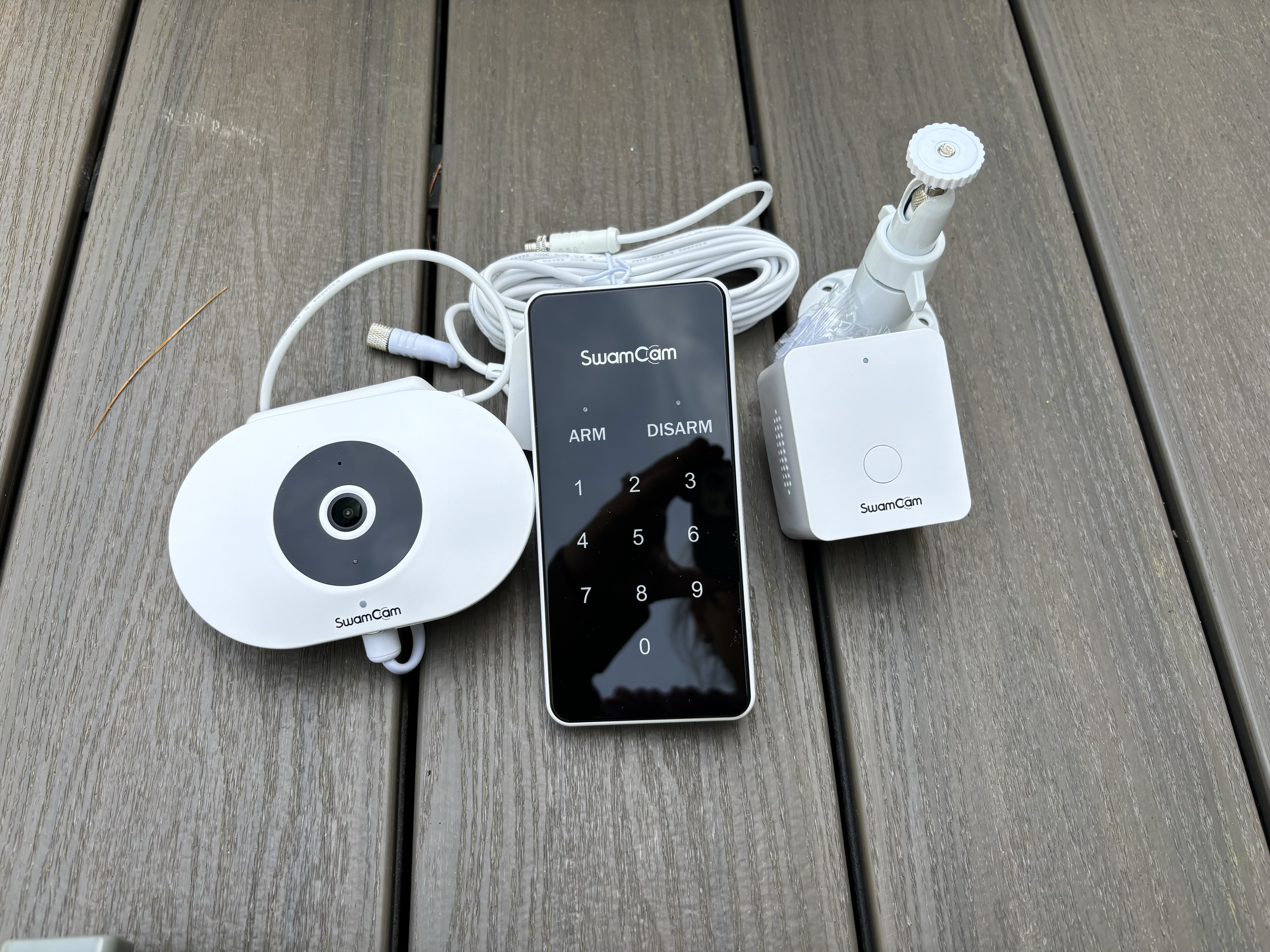 The included components of the SwamCam Camera Pool Alarm System on a pool deck before testing.