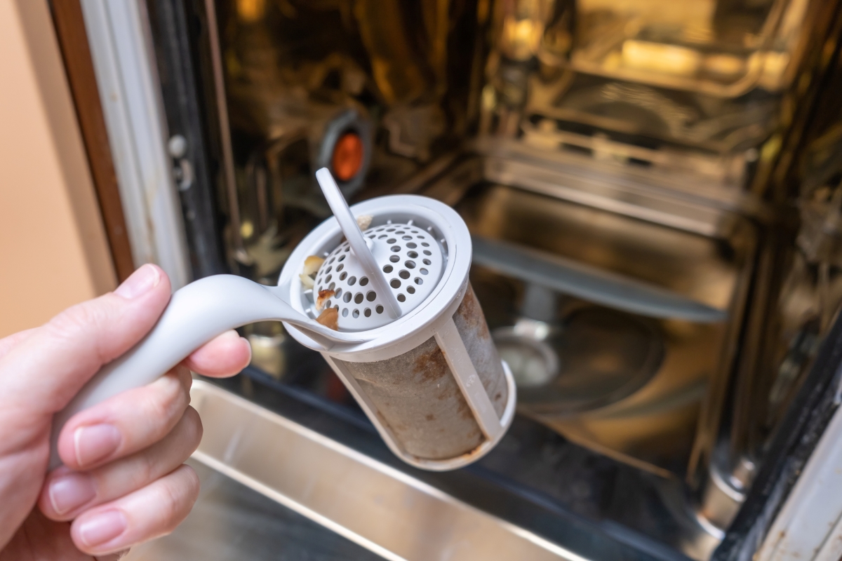 A person is holding a clogged drain basket from the dishwasher.