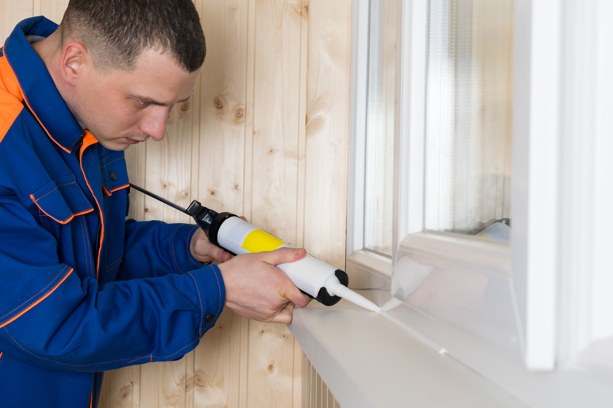 a man in clothes for repair seals the window cracks with selikon