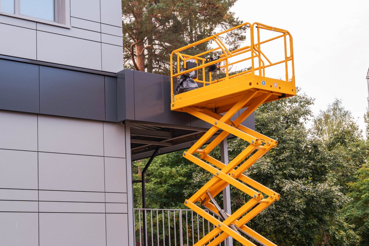 A view of a scissor lift next to a grey building. 