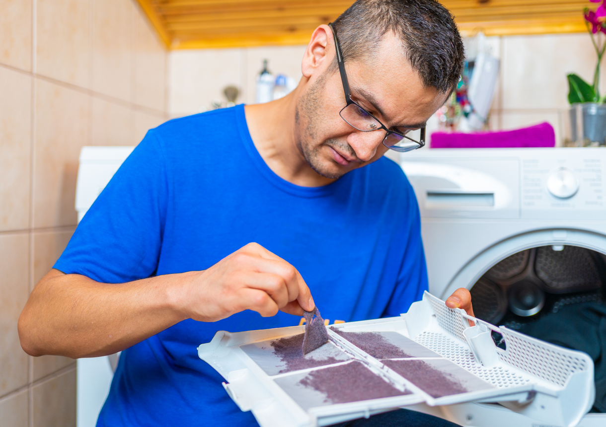 un jeune homme enlève les peluches du filtre à poussière du sèche-linge