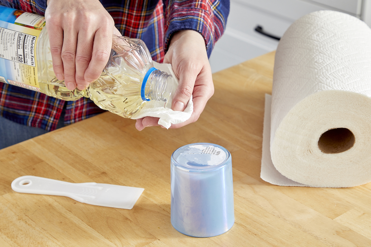 Woman uses cooking oil on a paper towel to remove a sticker from a cup.