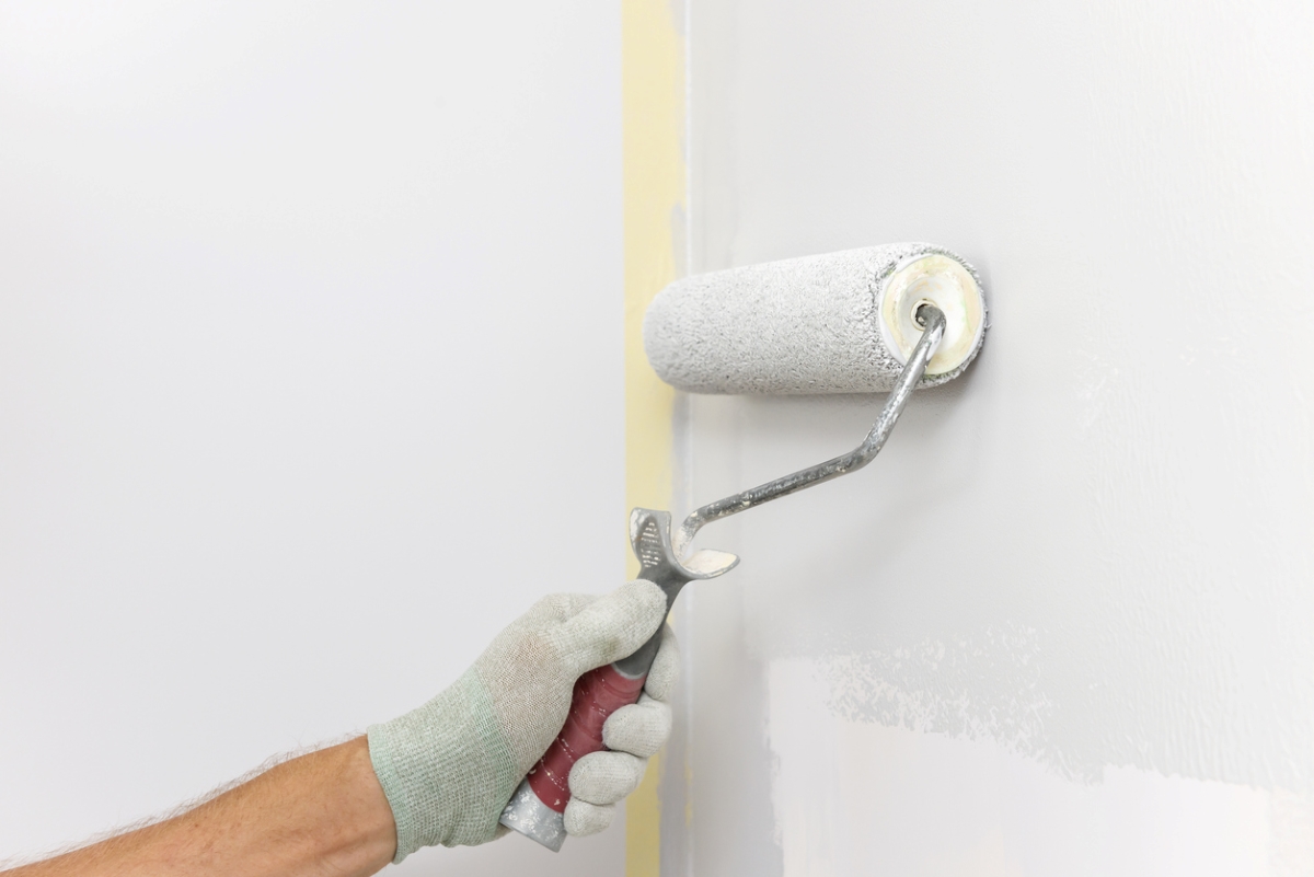 Gloved hand using roller to paint wall