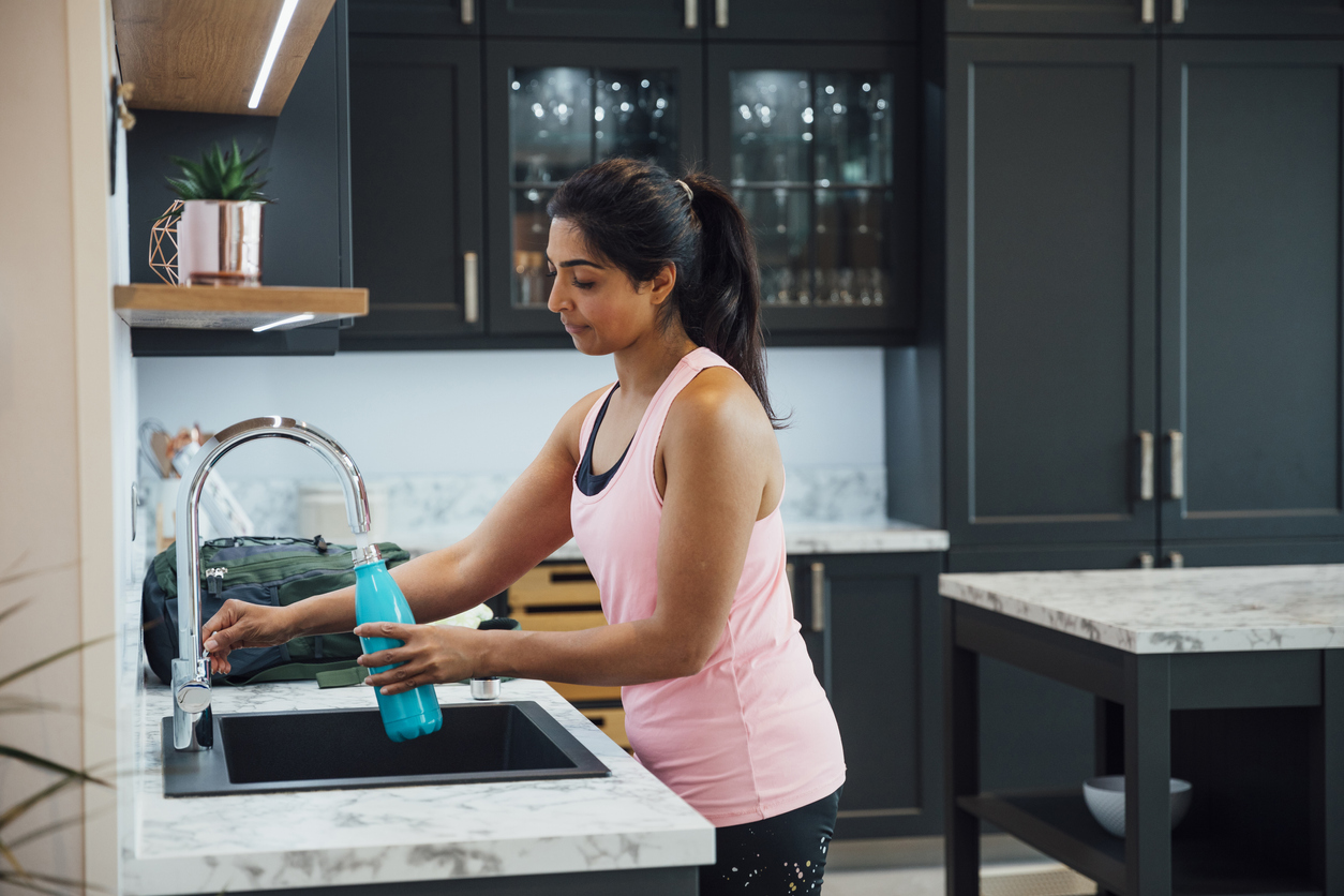 A woman in gym clothing prepares for the day and fills up her reusable water bottle before heading to the gym.