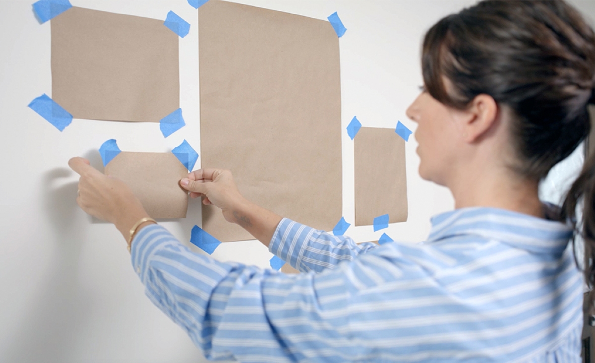 Woman using blue painters tape to hold picture placements on wall.