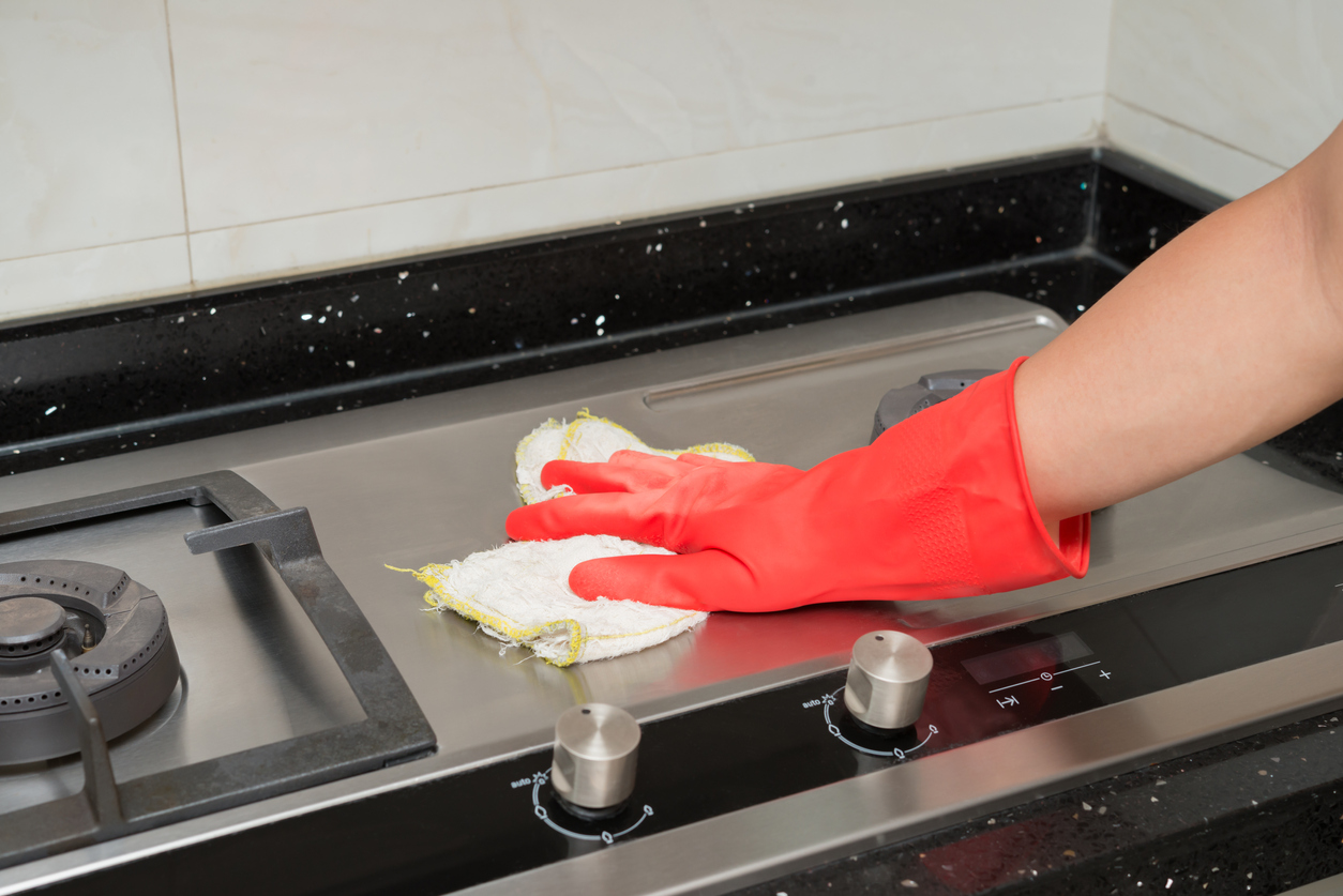 utilisation de l'huile de coco essuyer la cuisinière en acier inoxydable avec un chiffon portant des gants rouges