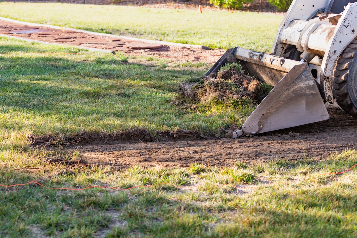 Un bulldozer enlève une pelouse résidentielle pour la remplacer par un aménagement paysager xéroscape.