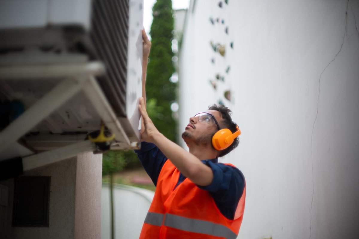 A worker in an orange safety vest inspects an AC unit.