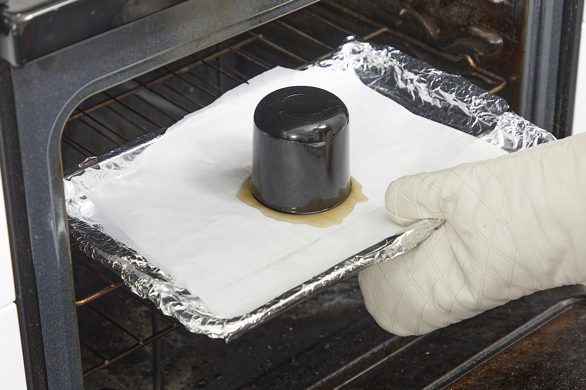 Taking baking sheet with upturned candle jar on it out of oven.