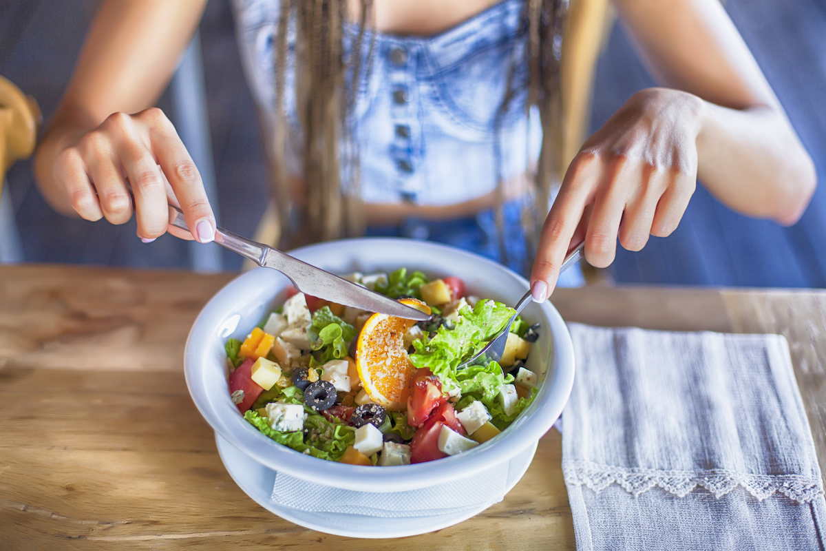 Young woman eating salad in restaurant, alone.