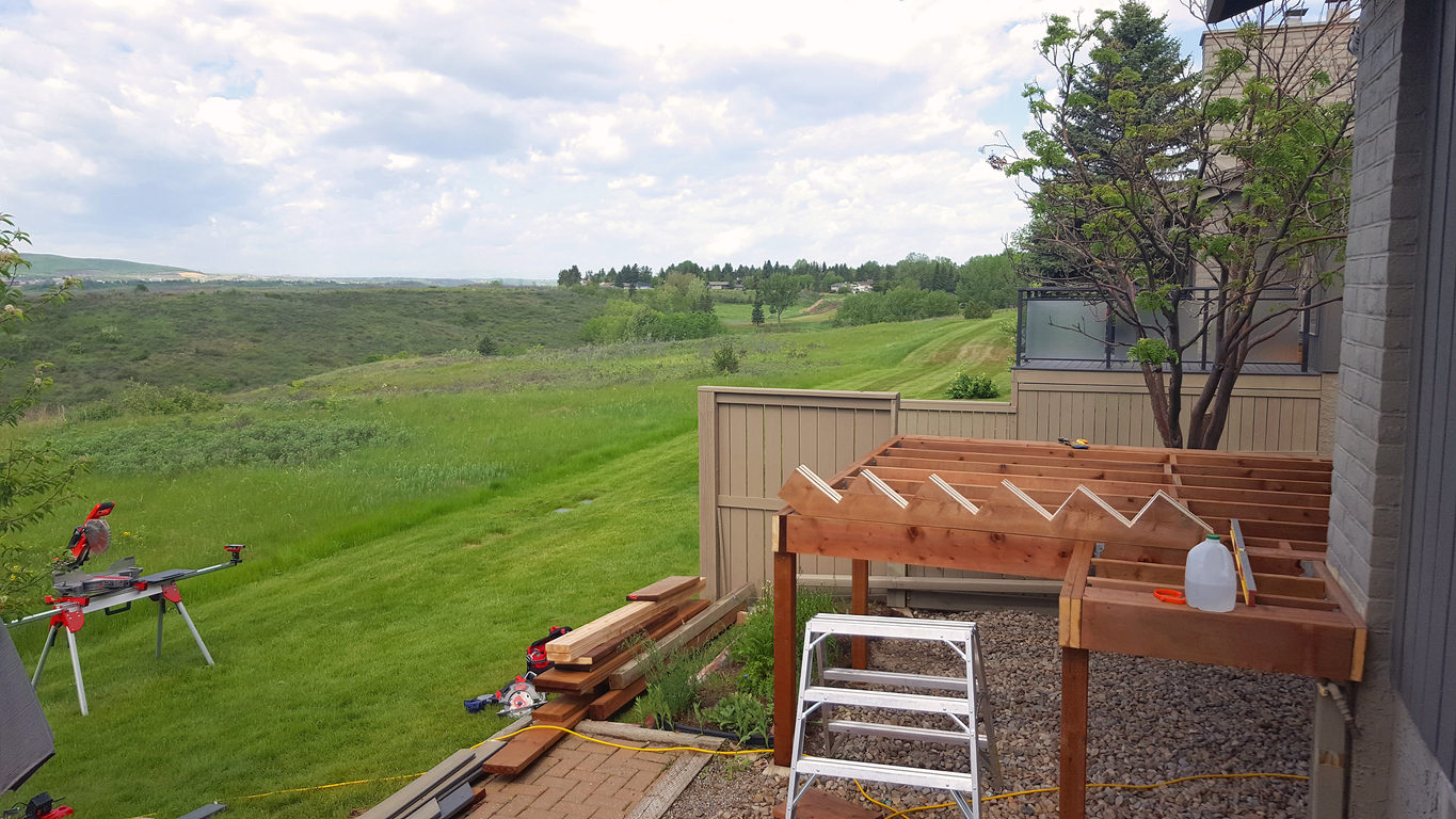 partially-constructed-deck-next-to-a-grey-house-in-a-green-valley