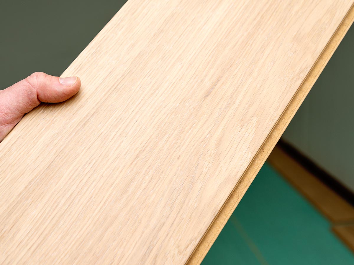 Une personne tenant un morceau de parquet contrecollé Flooret pendant l'installation et les tests.