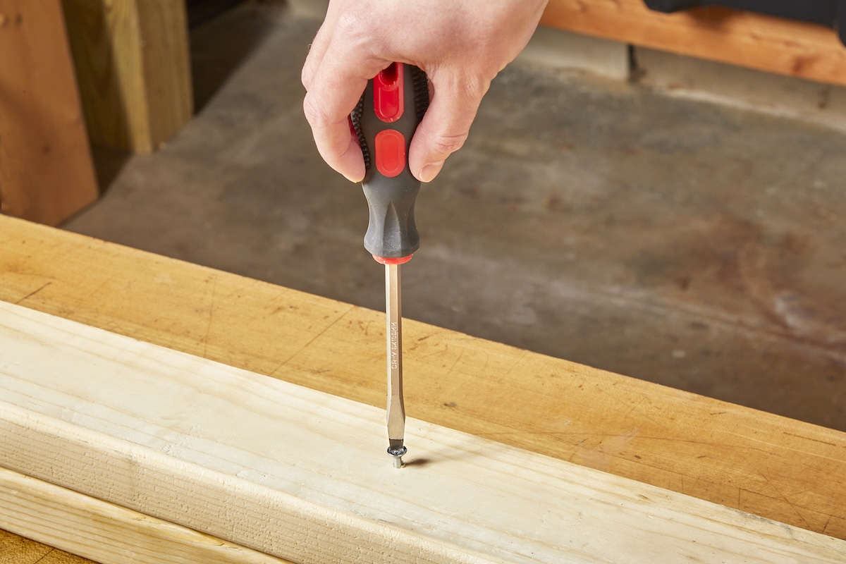 A person using a flathead screwdriver to remove a stripped screw stuck in a wood stud.