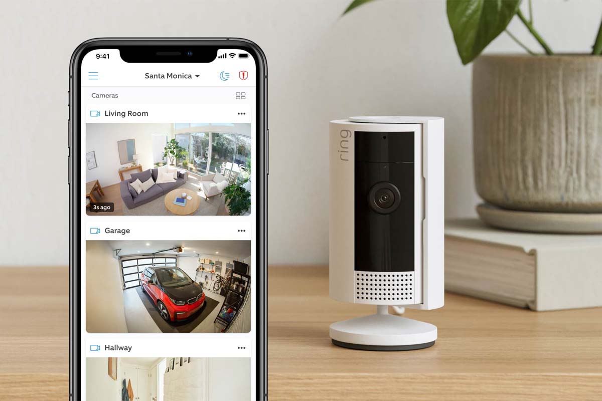 A Ring indoor camera sits on a table while the user views the Ring app on their phone.