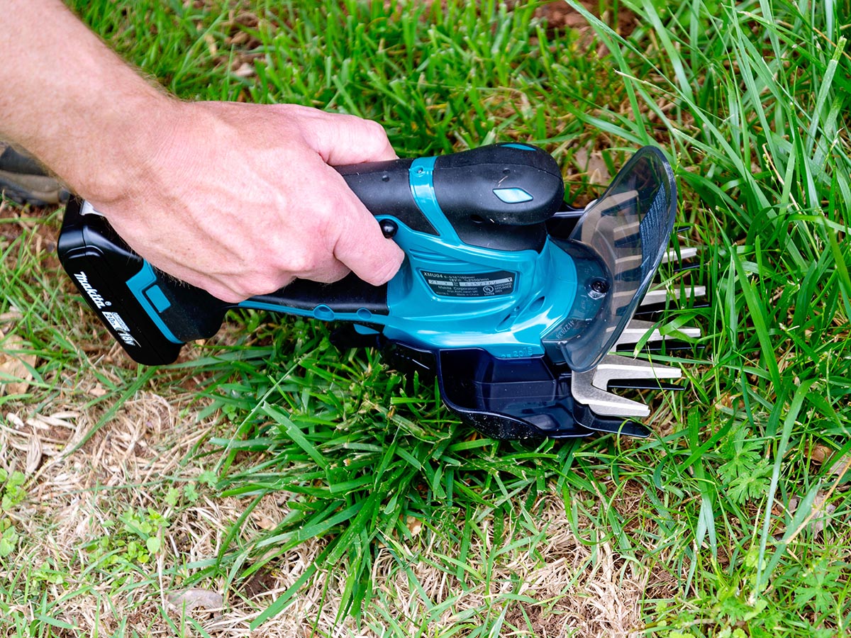 A hand holding the best cordless grass shears option and using it to trim grass