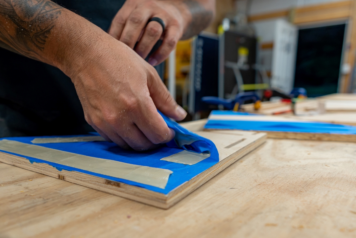 Person using blue tape to protect wooden frame.