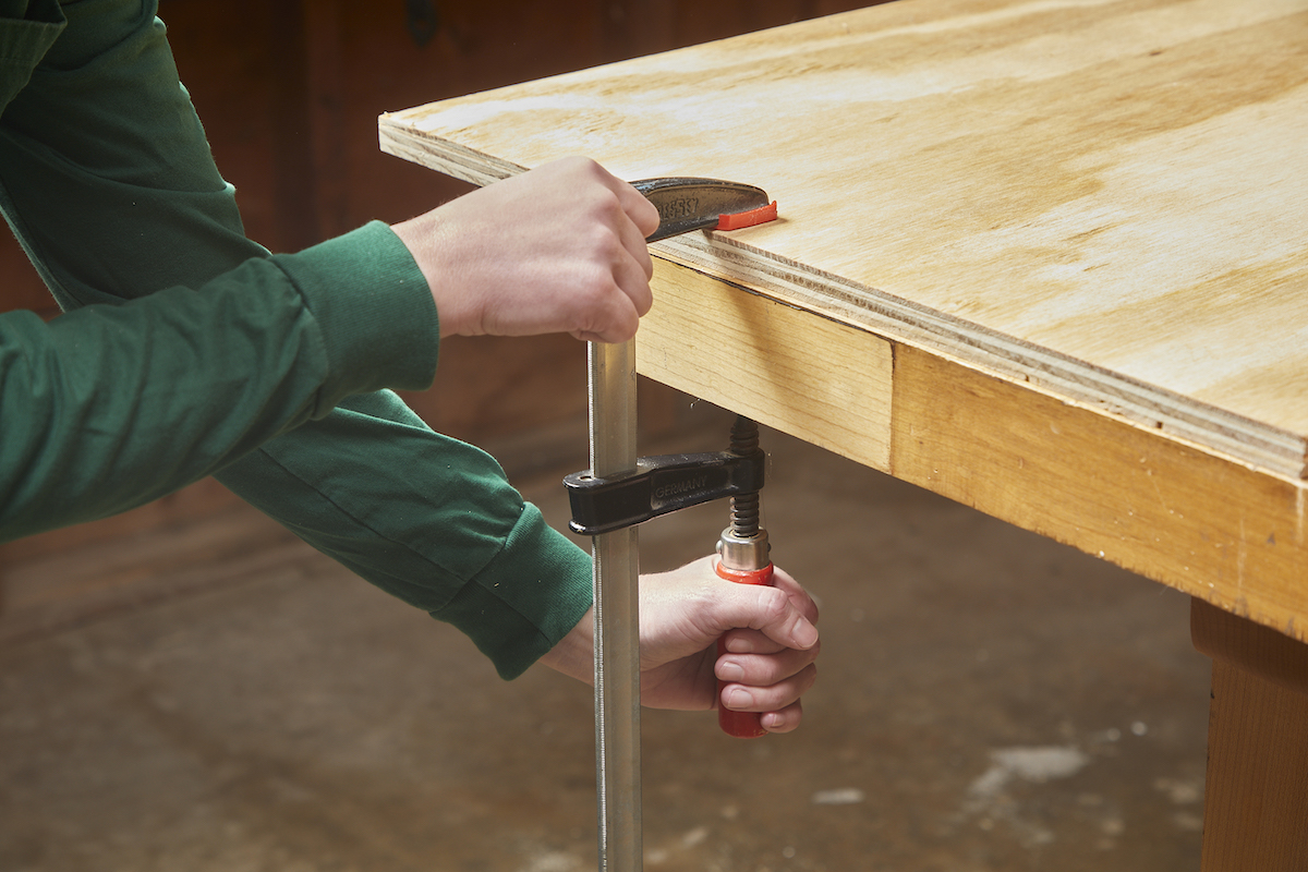 Une femme utilise une pince pour fixer du contreplaqué à une table de travail.