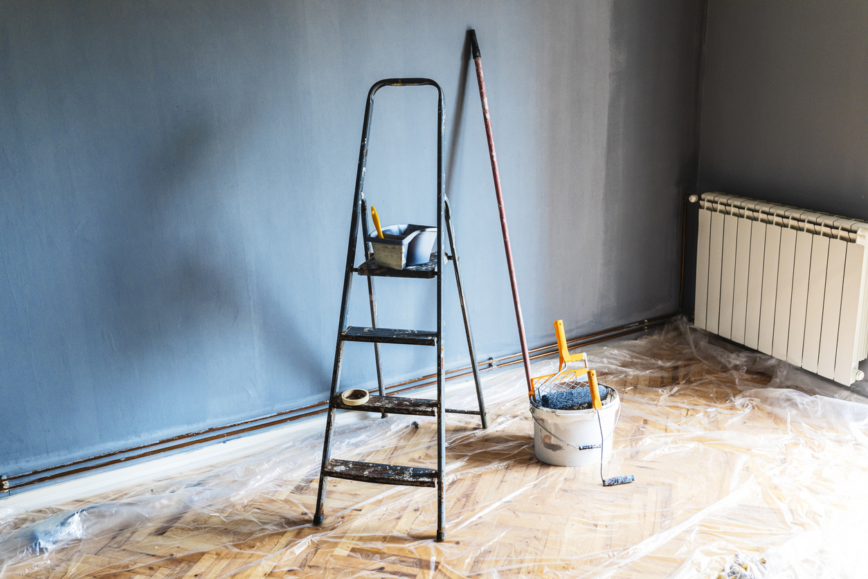 Painting tools and ladder in an empty room prepared for renovation with plastic tarp covering the floor.