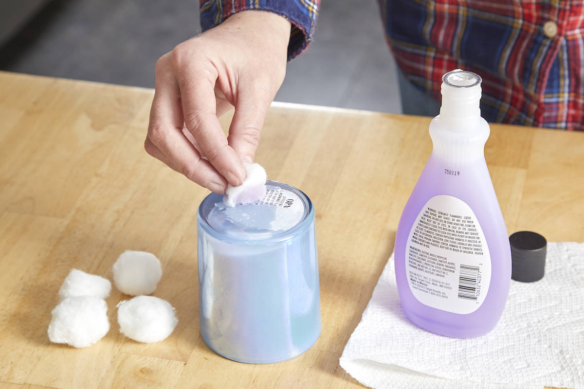 Woman uses nail polish remover on a cotton ball to remove a sticker on a candle jar.