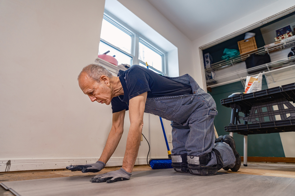 Senior Caucasian man doing construction renovation indoors. He is dressed in work clothes with jeans overall and t-shirt. Interior of private home during renovation, located in North America.