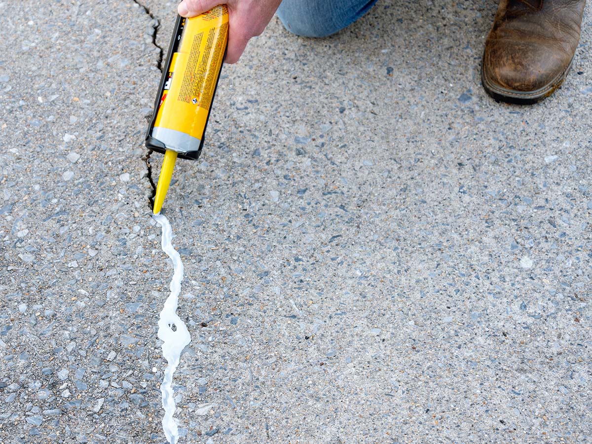 Une personne utilisant le scellant autonivelant Sikaflex pour combler une grande fissure dans le béton.