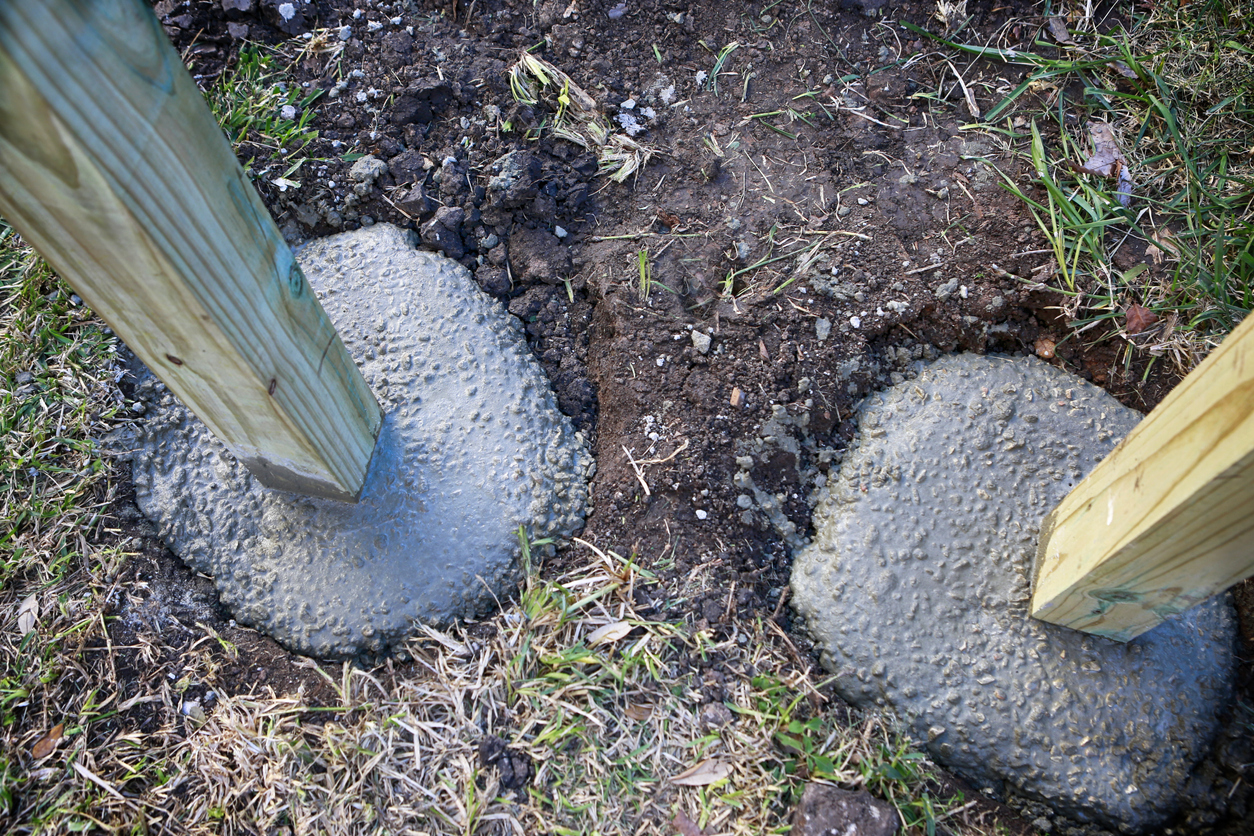 Building fence in progress: setting up wooden poles in concrete foundation.