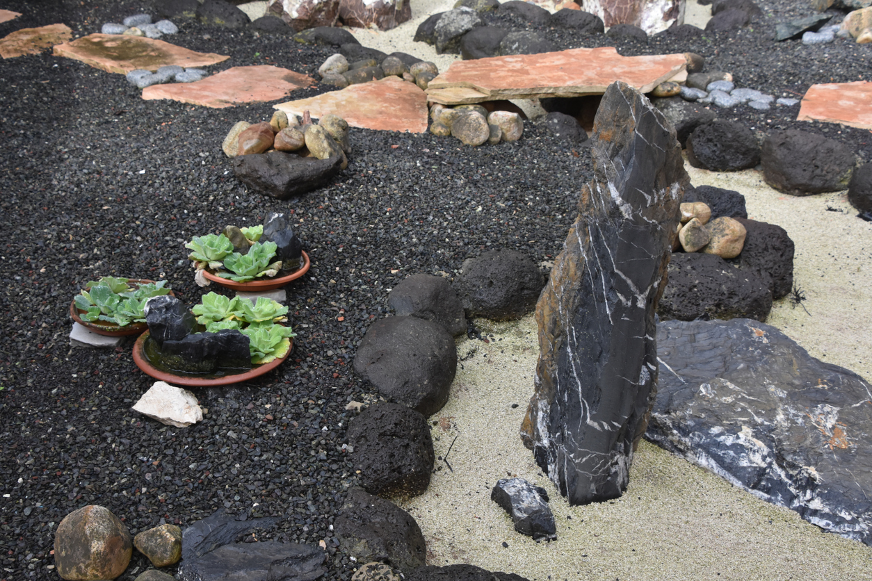 Jardin zen composé de sable, de plantes succulentes et de jardinières en terre cuite sur un lit de roches de lave.