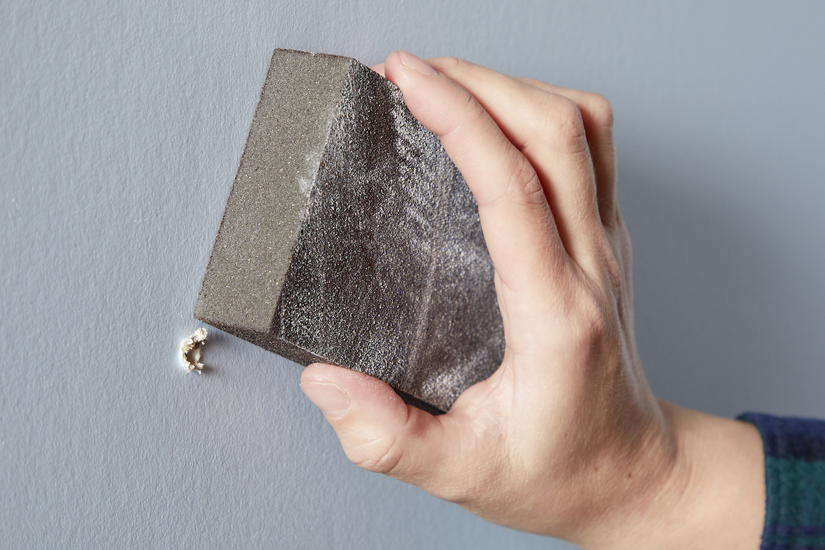 Woman using a sanding block to sand a small hole in drywall.