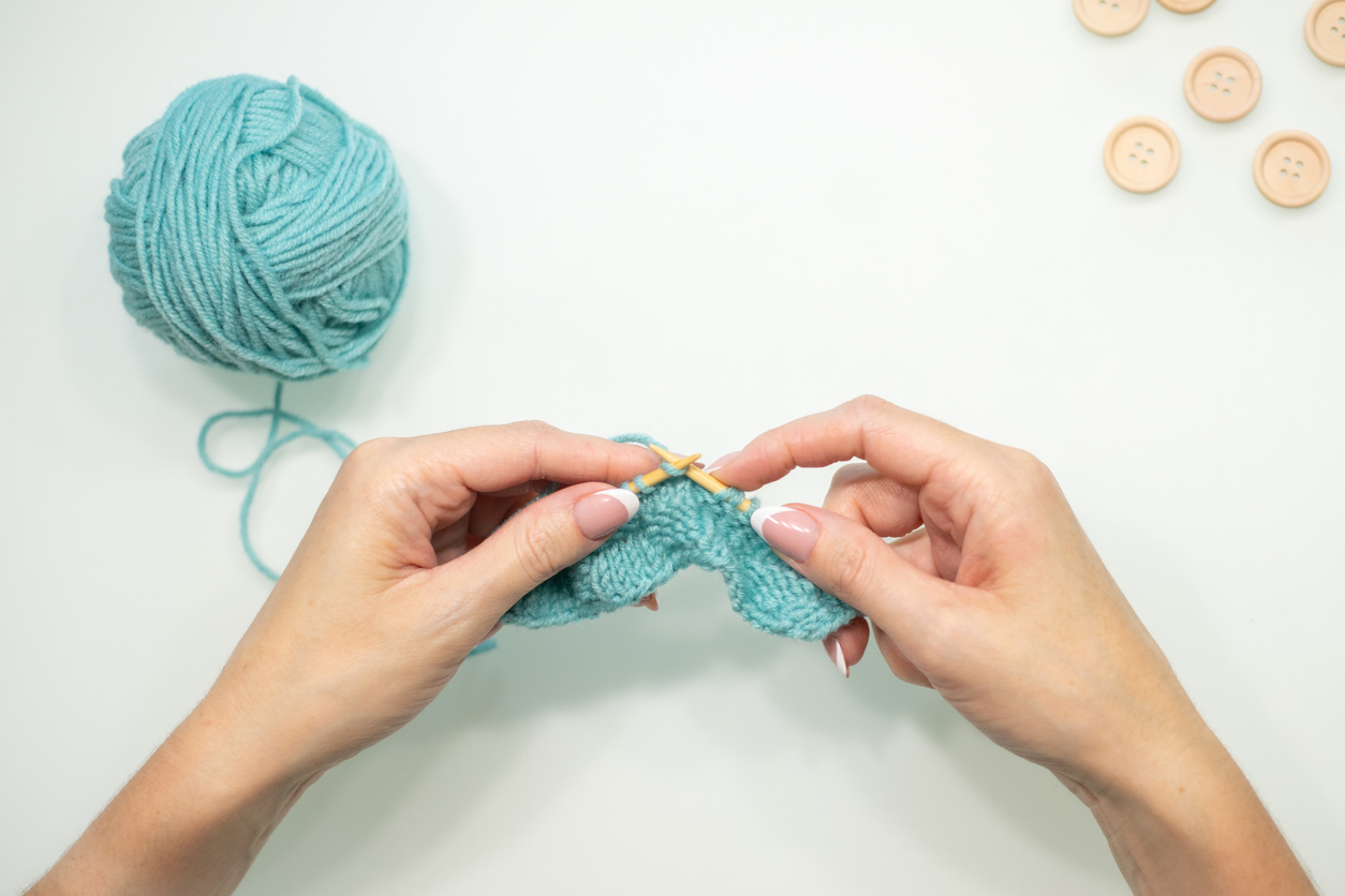 Hands showing how to hold knitting needles with the pencil grip