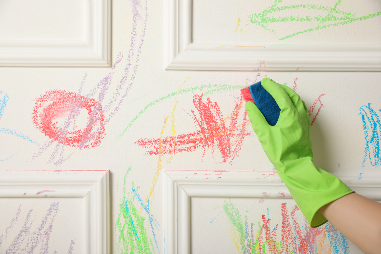 nettoyer les marques de crayon colorées sur le mur en portant des gants verts avec une éponge