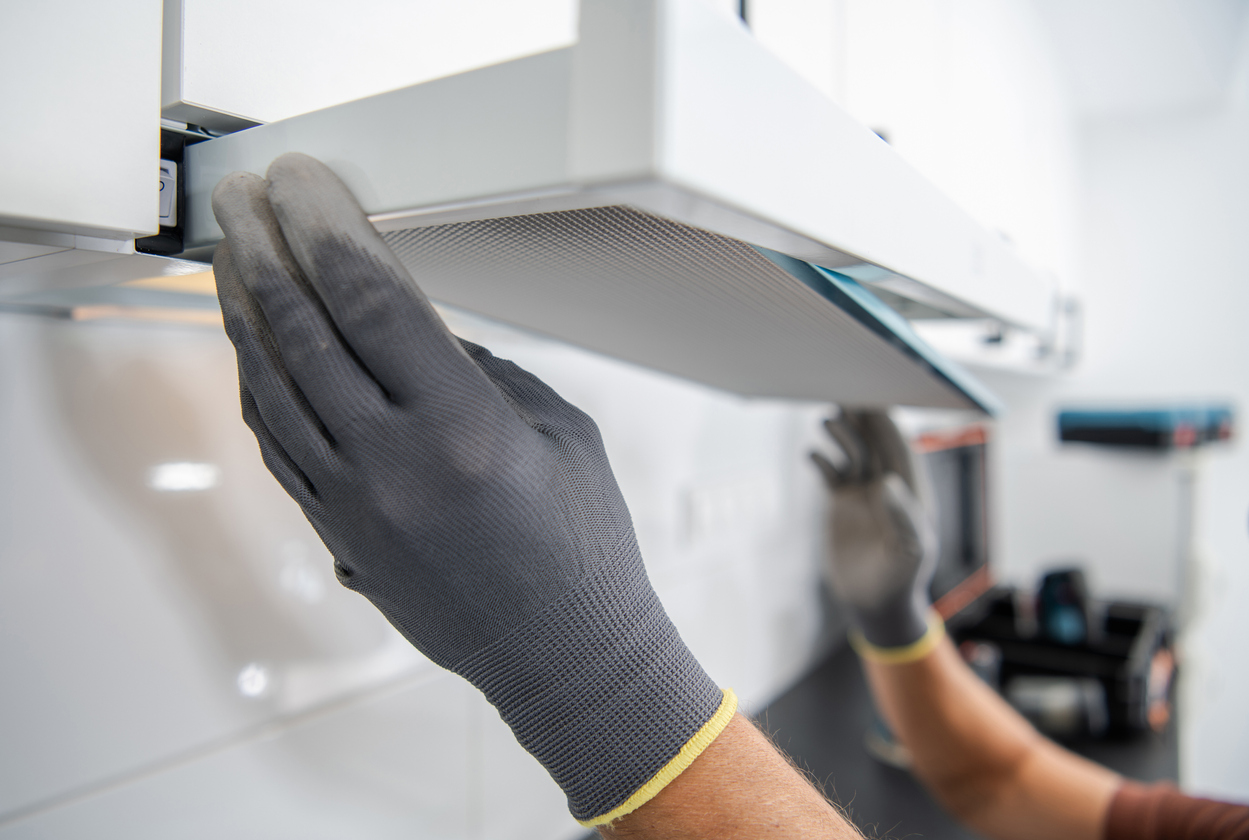 gros plan du filtre de la hotte de cuisinière retiré par deux mains avec des gants gris