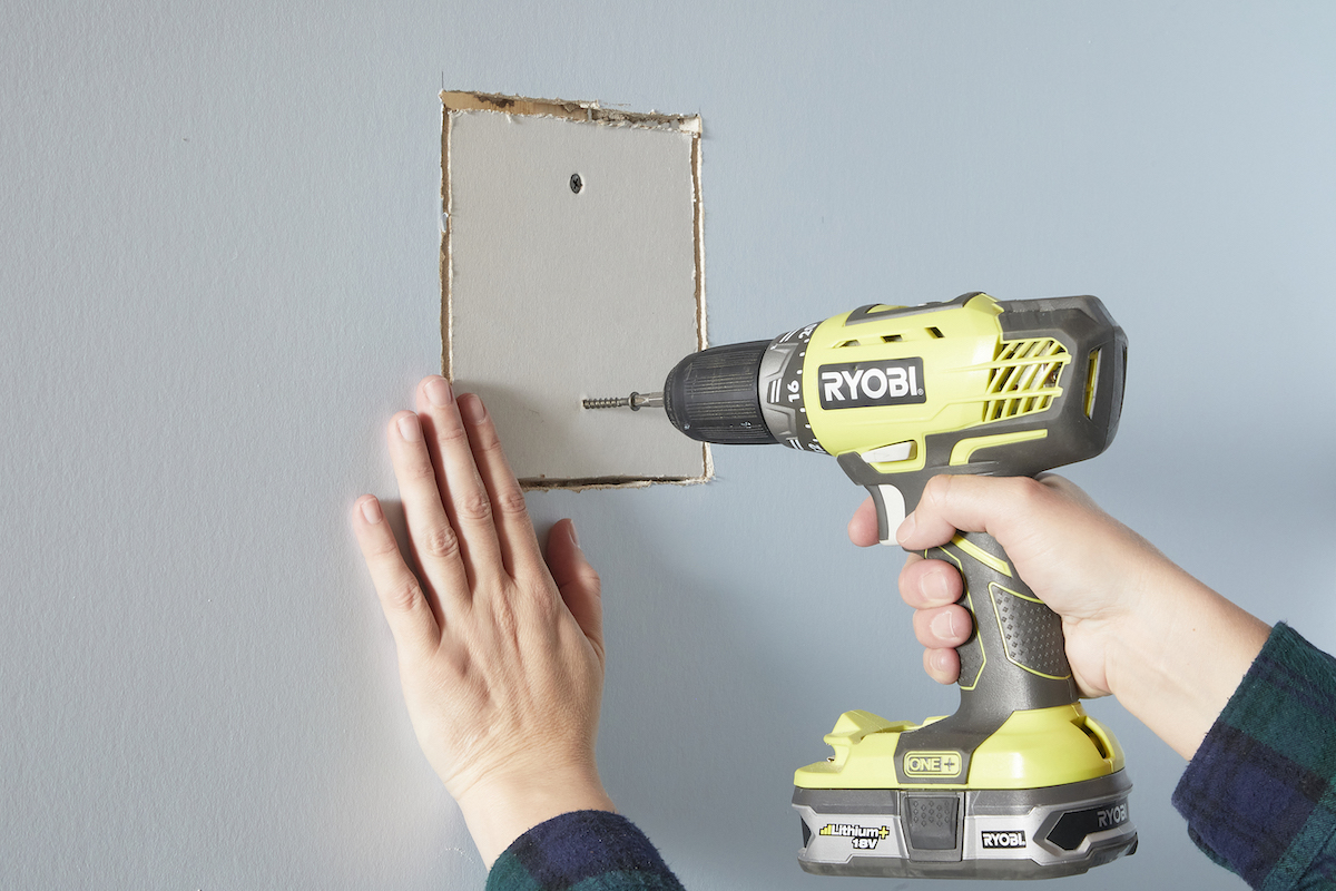 Woman uses drywall screws to attach drywall patch to wall stud.