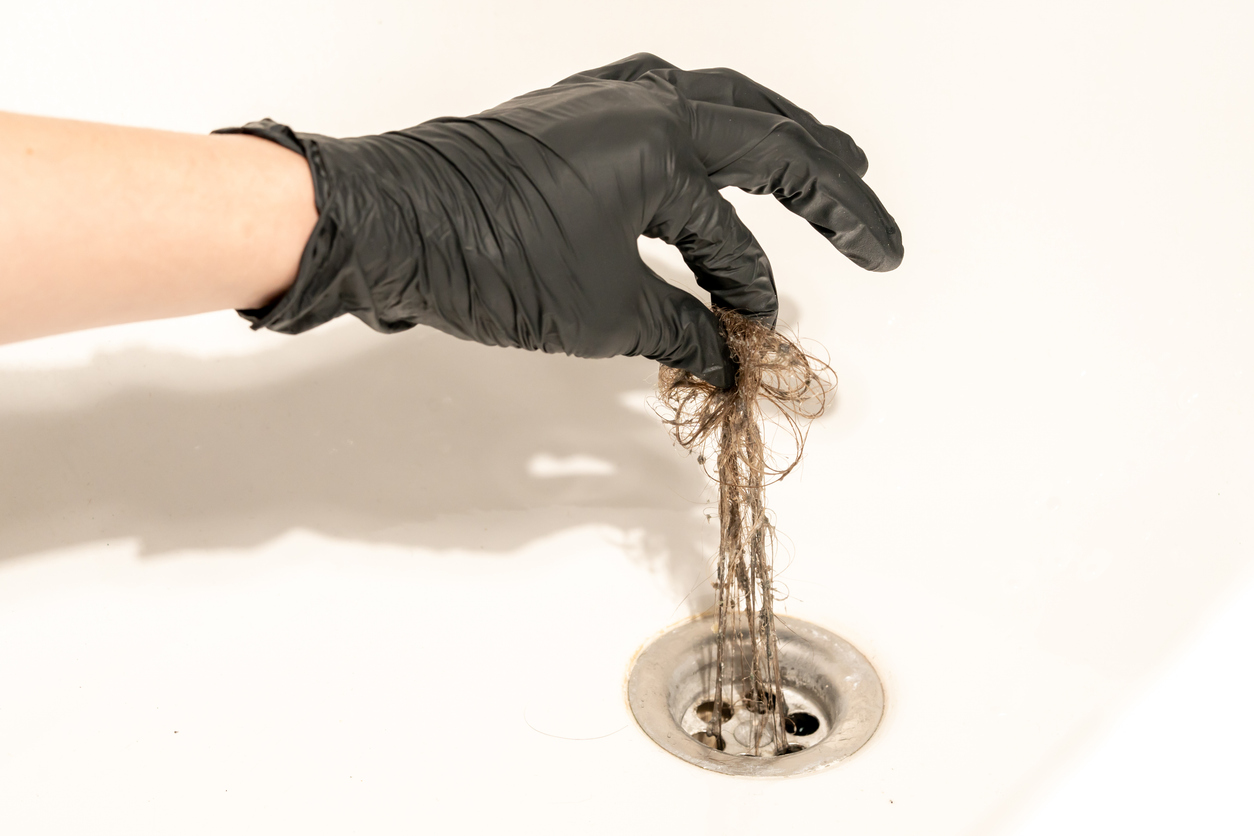 Une personne portant un gant en caoutchouc noir nettoie les cheveux du drain de la douche.