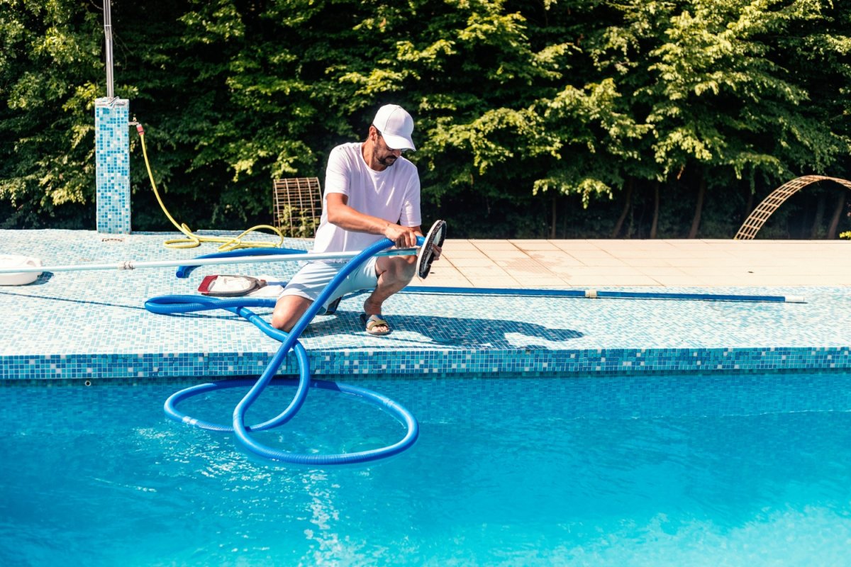 A man uses a tool to clean a pool.