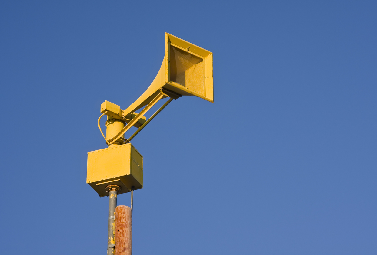 Outdoor warning siren with a blue sky in the background.