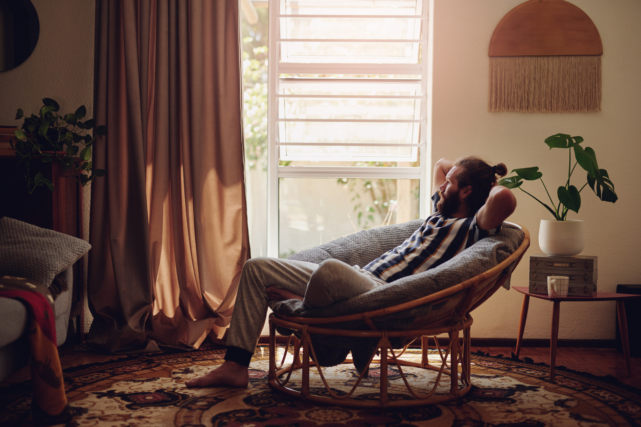 young bearded man with man bun relaxes in modern living room with long puddle curtains in window