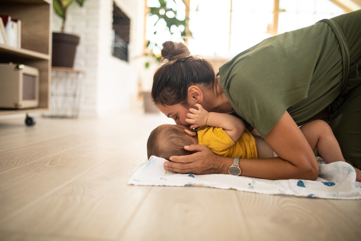 A mother is playing with her baby on the light wood colored laminate floor.