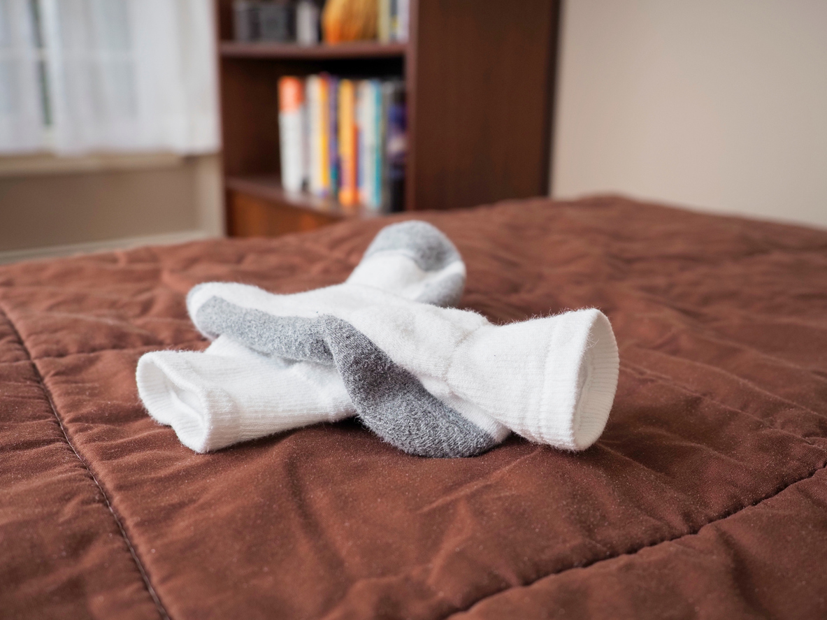 Le froid hivernal peut nécessiter de porter des chaussettes au lit pour garder vos pieds au chaud, un concept hivernal. Des chaussettes blanches sont posées sur une couette marron sur un lit dans une chambre à coucher domestique. D'autres meubles de la chambre restent flous en arrière-plan, notamment une bibliothèque.