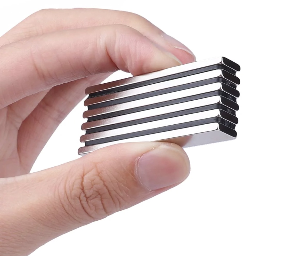 Person holding a stack of neodymium magnets against a white wall.